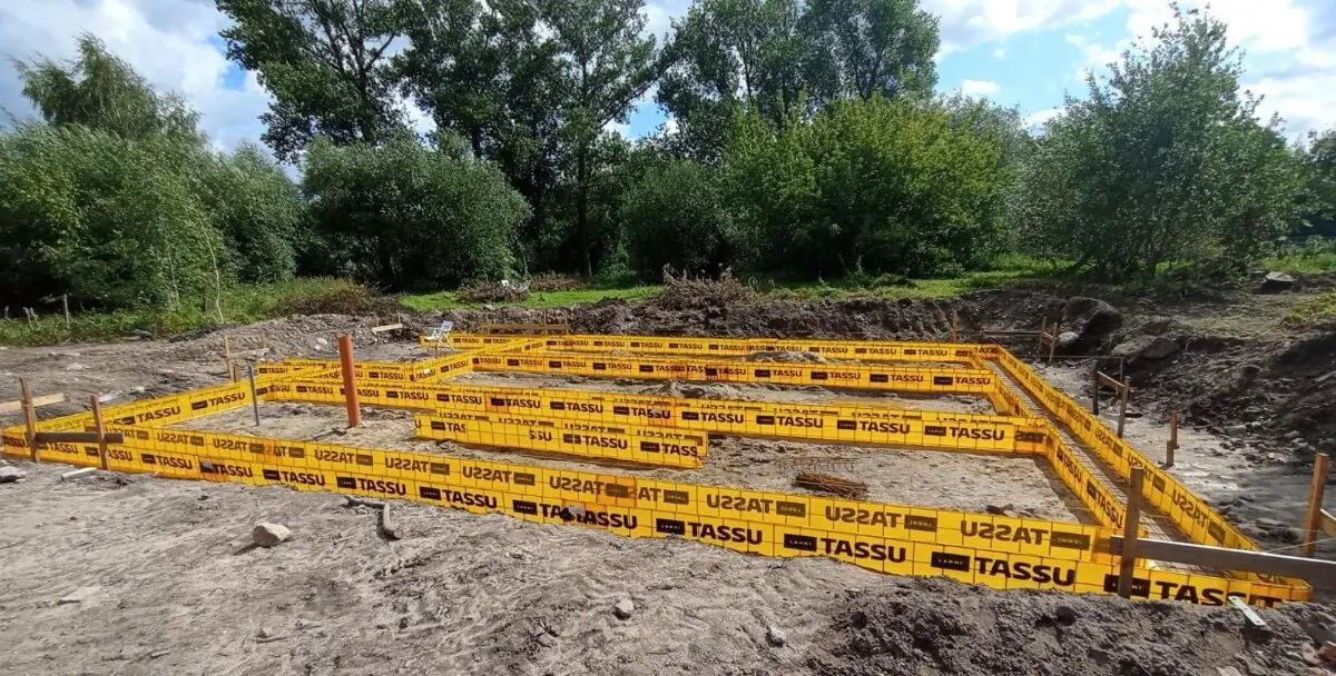 Żółte szalunki ław fundamentowych ustawione na wyrównanym gruncie, w tle drzewa